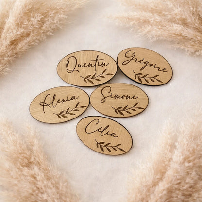 Marque-place en bois personnalisé 7x4 cm avec prénom en écriture calligraphique et motif feuillage. Idéal pour mariage et événement.